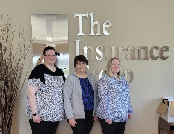 Kim, Lynn, and Tasha standing beside The Insurance Group sign in the office